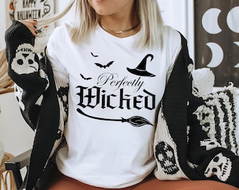 May include: White t-shirt with the phrase "Perfectly Wicked" in black gothic lettering, a witch hat, bats, and a broom. The person is wearing a black and white patterned cardigan. Halloween themed apparel.