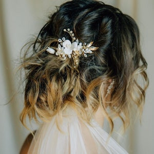 May include: A white bridal veil with a delicate floral hair comb featuring white flowers and gold accents.