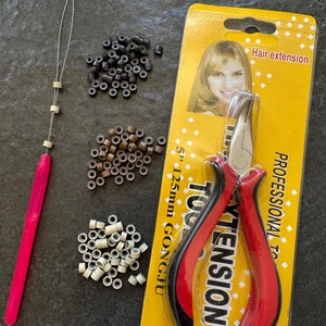 May include: A set of hair extension tools including a pair of pliers, a needle tool, and three bags of micro rings in black, brown, and blonde colors. The packaging for the pliers says "Hair extension tools" and "Professional tools".