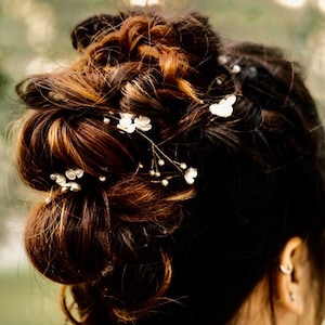 May include: A woman's brown hair is styled in a messy bun with small white flower hair clips. The hair clips are scattered throughout the bun.