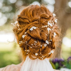 May include: A woman with red hair wearing a white veil and a delicate floral hairpiece with small white flowers and pearls.