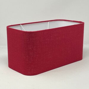 May include: A rectangular red lampshade made of fabric. The lampshade has a white interior.