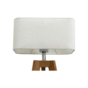 May include: A contemporary table lamp with a rectangular, cream-coloured fabric shade. The lamp has a chrome stem and a wooden tripod base. The shade is approximately 46 cm long and 25 cm wide. Suitable for indoor use.