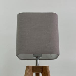 May include: A grey fabric lampshade with a chrome base and a wooden tripod stand.