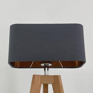 May include: A grey rectangular lampshade with a copper trim sits atop a wooden tripod lamp base.