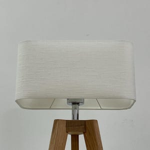 May include: A white rectangular lampshade with a chrome base and three wooden legs.
