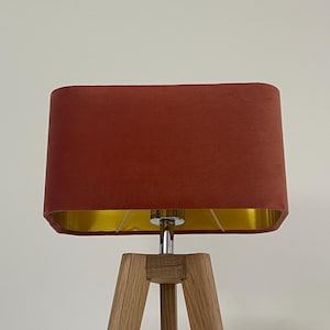 May include: A red velvet lampshade with a gold trim sits atop a wooden tripod floor lamp.
