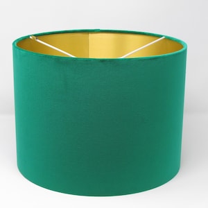 May include: A green velvet lampshade with a gold lining. The lampshade is cylindrical in shape and has a white cord.