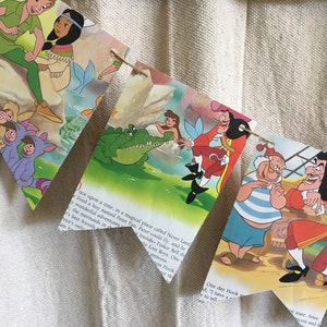 K&ouml;nnte beinhalten: Ein farbenfrohes Banner zum Thema Peter Pan mit Bildern von Peter Pan, Captain Hook, Tinkerbell und den Verlorenen Jungen. Das Banner ist aus Papier und hat eine Schnur, die durchgezogen ist.