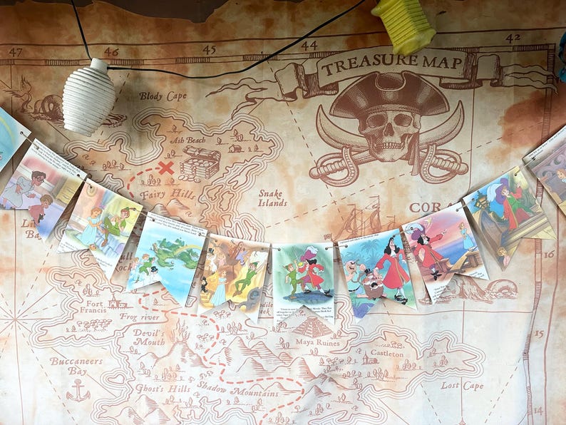 K&ouml;nnte beinhalten: Ein farbenfroher Papierbanner mit Illustrationen von Figuren aus Peter Pan. Der Banner ist an einer schwarzen Schnur befestigt und h&auml;ngt vor einem braunen Hintergrund mit einer darauf gedruckten Schatzkarte. Die Karte zeigt einen Totenkopf mit gekreuzten Knochen und die Worte "TREASURE MAP".