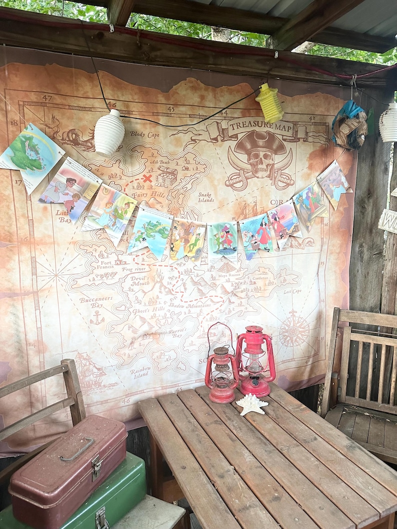 K&ouml;nnte beinhalten: Ein Holztisch mit zwei roten Laternen, einem Seestern und zwei Metallwerkzeugk&auml;sten. Hinter dem Tisch h&auml;ngt eine Piraten-Tapete an der Wand, die eine Schatzkarte mit dem Text "TREASURE MAP" und einem Totenkopf mit Knochen zeigt.