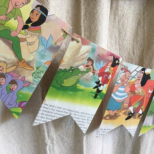 K&ouml;nnte beinhalten: Ein farbenfrohes Peter-Pan-Banner mit Bildern von Peter Pan, Tinkerbell, Captain Hook und dem Krokodil. Das Banner ist aus Papier und hat eine Schnur, die durchl&auml;uft.