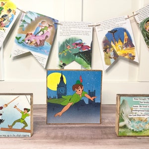 K&ouml;nnte beinhalten: Drei Holzbl&ouml;cke mit Illustrationen und Text aus der Peter Pan Geschichte. Der mittlere Block zeigt Peter Pan, der mit Big Ben im Hintergrund fliegt. Der Block links zeigt Peter Pan, der gegen Captain Hook k&auml;mpft. Der Block rechts zeigt eine Szene aus der Geschichte mit dem Text "Peter brachte Wendy und ihre Br&uuml;der zu seinem Haus. Er lebte in einem geheimen unterirdischen Versteck mit den Verlorenen Jungen und Tinkerbell."