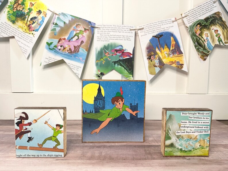 K&ouml;nnte beinhalten: Drei Holzbl&ouml;cke mit Illustrationen und Text aus der Peter Pan Geschichte. Der mittlere Block zeigt Peter Pan, der mit Big Ben im Hintergrund fliegt. Der Block links zeigt Peter Pan, der gegen Captain Hook k&auml;mpft. Der Block rechts zeigt eine Szene aus der Geschichte mit dem Text "Peter brachte Wendy und ihre Br&uuml;der zu seinem Haus. Er lebte in einem geheimen unterirdischen Versteck mit den Verlorenen Jungen und Tinkerbell."