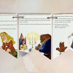 May include: A decorative recipe card set featuring Disney princesses. The cards are connected with twine and showcase illustrations of Mulan, Aurora, Belle, Cinderella, and Snow White. Each card displays a recipe with accompanying images.