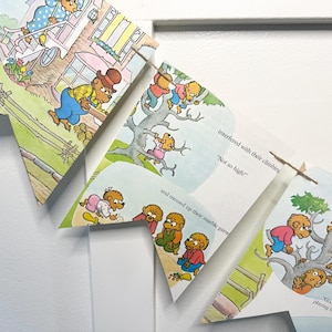 May include: A children's book page banner featuring illustrations of bears in various scenes. The pages are cut into arrow shapes and strung together, displaying colorful images and text from the story.