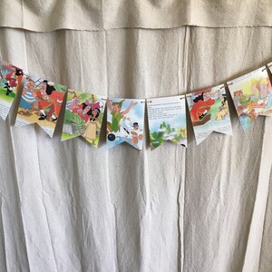 K&ouml;nnte beinhalten: Ein Peter-Pan-Partybanner mit Illustrationen aus dem Buch. Der Banner zeigt Peter Pan, Captain Hook und andere Figuren aus der Geschichte. Der Banner ist aus Papier und mit einer Schnur zusammengef&uuml;gt.