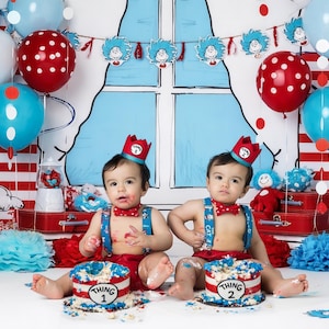 Könnte beinhalten: Geburtstagsszene mit zwei Babys, die jeweils eine Krone und eine Fliege tragen und vor Kuchen mit der Aufschrift "Thing 1" und "Thing 2" sitzen. Rote, weiße und blaue Luftballons sowie Dekorationen im Stil von Dr. Seuss schaffen eine festliche Atmosphäre.