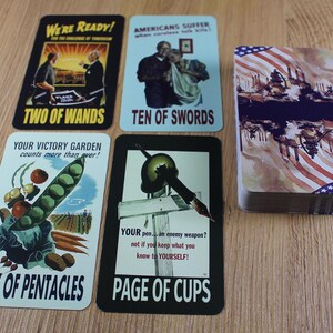 Puede incluir: Una baraja de cartas de juego de estilo vintage con ilustraciones patri&oacute;ticas y de propaganda. Las cartas presentan im&aacute;genes y texto, incluyendo "Two of Wands", "Ten of Swords", "Six of Pentacles" y "Page of Cups". La baraja est&aacute; apilada junto a cartas individuales.