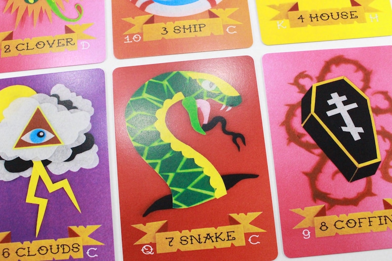Puede incluir: Un juego de cartas con ilustraciones coloridas. Las cartas representan un tr&eacute;bol, un barco, una casa, nubes, una serpiente y un ata&uacute;d. Las cartas est&aacute;n numeradas del 2 al 9 y tienen una designaci&oacute;n alfab&eacute;tica.