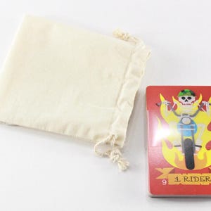 Puede incluir: Una carta de juego roja con un esqueleto montando una motocicleta a trav&eacute;s de las llamas. La carta est&aacute; numerada con el n&uacute;mero 9 y tiene el texto "1 Rider". La carta forma parte de una baraja de cartas y viene con una bolsa de cord&oacute;n blanco.