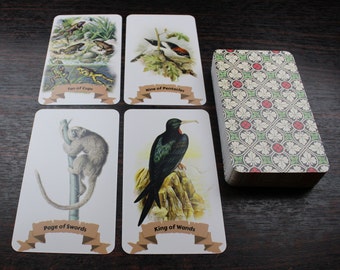 Puede incluir: Un juego de cartas de tarot con ilustraciones de animales y naturaleza. Las cartas están dispuestas en una cuadrícula sobre una superficie de madera. Las cartas incluyen el Diez de Copas, el Nueve de Pentáculos, el Paje de Espadas, el Rey de Varitas y una baraja de cartas con un patrón verde y rojo.