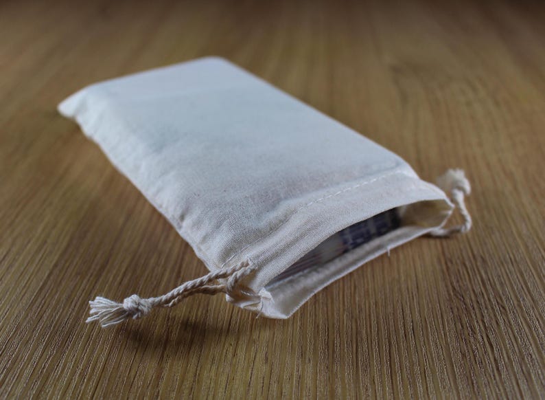 Puede incluir: Una peque&ntilde;a bolsa rectangular de lona blanquecina con cierre de cord&oacute;n. La bolsa est&aacute; sobre una superficie de madera. La bolsa est&aacute; ligeramente abierta, revelando una vista del contenido.