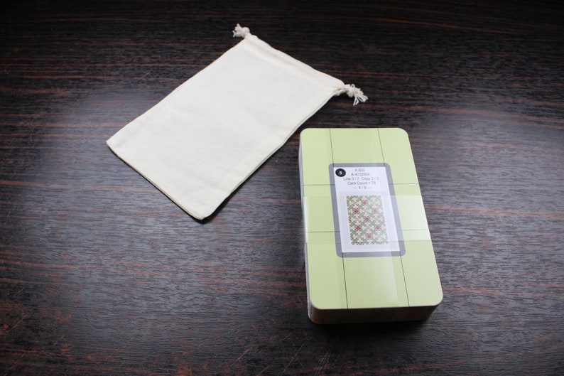 Op de afbeelding: Een groene en witte quiltliniaal met een rasterpatroon en een klein kaartje met een quiltblokdesign. De liniaal is verpakt in een witte trekkoordtas.
