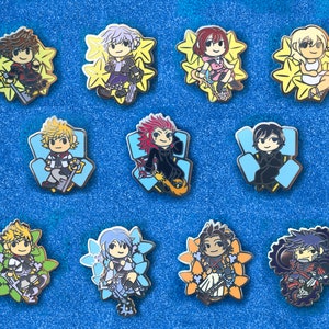May include: Ten enamel pins featuring characters from the Kingdom Hearts video game series. The pins are colorful and feature various characters, including Sora, Riku, Kairi, and others. Each pin is approximately 1 inch in diameter.