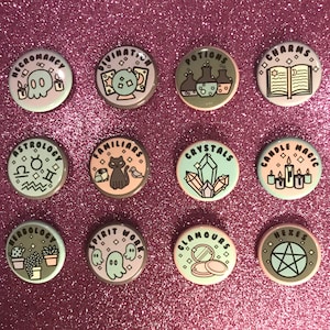 Puede incluir: Doce botones redondos con fondos de color pastel y contornos negros. Cada botón presenta un tema de brujería diferente, que incluye necromancia, adivinación, pociones, encantos, astrología, familiares, cristales, magia de velas, herbología, trabajo espiritual, encantos y hechizos.