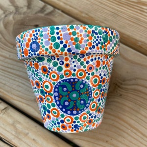 May include: A white terracotta flower pot with a hand-painted design of orange, blue, green, and purple dots and circles.