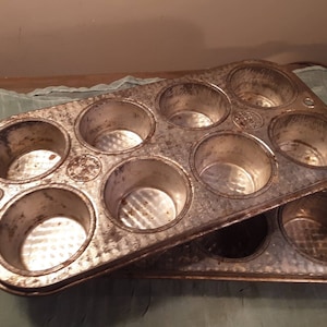 May include: A vintage metal muffin tin with 12 individual cups. The tin is worn and has a rustic look.