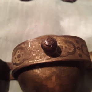 May include: Two antique brass bells with a decorative embossed design and a wooden knob on top.