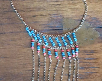 May include: A gold chain necklace with a blue and coral bead fringe. The necklace has a delicate chain and a layered fringe of beads.