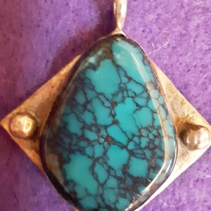 May include: A turquoise gemstone pendant with a silver setting. The stone has a unique pattern of black veins.