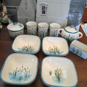 May include: Set of white ceramic bowls with blue and green floral designs. The bowls are square and have a speckled glaze. There are also four small cups and a sugar bowl with the same design.