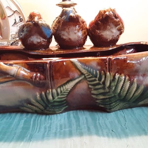 May include: A brown ceramic planter with a raised design of bamboo and ferns. Three small ceramic birds are perched on the top of the planter.