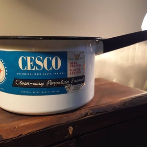 May include: White enamel saucepan with a black handle and a blue and white label that reads "CESCO, Columbian, Terre Haute, Indiana, Since 1921, Heat Saving Flavor Saving, Clean-easy Porcelain Enamel, General Steel Wares Limited".