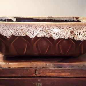 May include: A brown ceramic planter with a white glaze. The planter has a rectangular shape with a slightly rounded bottom and a geometric pattern around the rim.