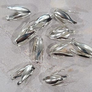 May include: A group of ten silver-toned metal bead caps. The caps are shaped like a flower with a small opening at the top.