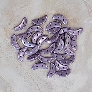 May include: A pile of small, crescent-shaped beads in a light purple color with a metallic sheen.