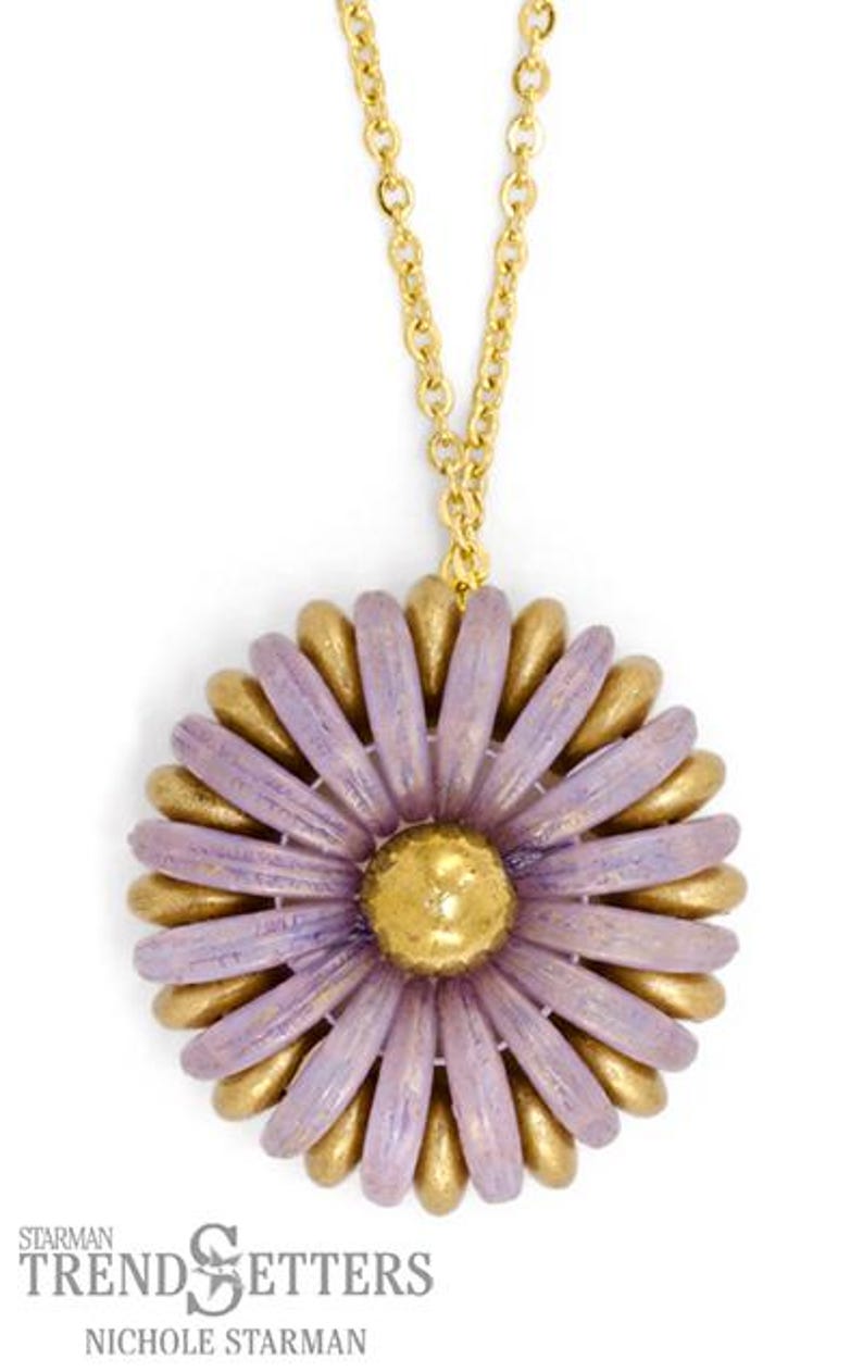 May include: A gold chain necklace with a purple and gold flower pendant. The flower has a textured, layered look and is made of polymer clay.