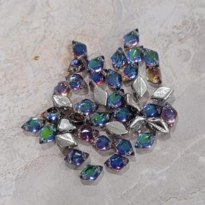 May include: A collection of iridescent blue and purple glass beads in a diamond shape. The beads are scattered on a white surface.