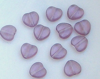 May include: A collection of 12 heart-shaped beads in a light purple color. The beads are made of glass and have a slightly iridescent finish.
