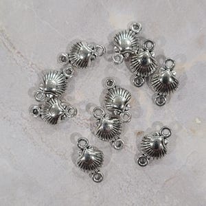 May include: A collection of silver-toned metal charms shaped like seashells. Each charm has two loops for attaching to jewelry or other crafts.