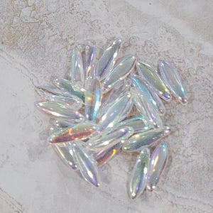May include: A pile of iridescent glass beads in various shapes and sizes. The beads are a mix of clear and opalescent colors, with a rainbow sheen.