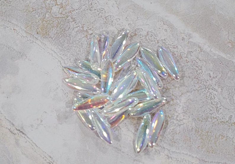 May include: A pile of iridescent glass beads in various shapes and sizes. The beads are a mix of clear and opalescent colors, with a rainbow sheen.