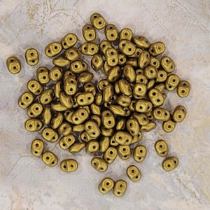 May include: A pile of gold-colored glass beads with two holes in each bead. The beads are small and have a matte finish.