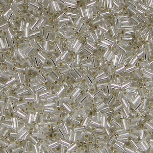 May include: Close-up of a pile of clear, rectangular beads with a silver metallic finish. The beads are scattered, showing their cylindrical shape and the small holes for stringing. Ideal for jewelry making and crafts.