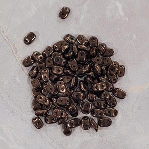 May include: A pile of small, dark brown glass beads with two holes in each bead.